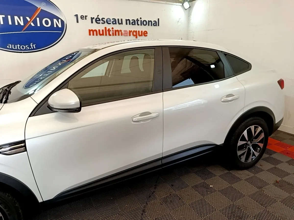 Profil côté gauche du Renault Arkana blanc 2023 avec jantes bicolores et lignes de caisse marquées.