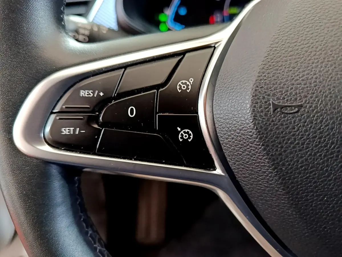 Gros plan sur les commandes de régulateur de vitesse au volant cuir du Renault Arkana blanc, version Evolution E-Tech.