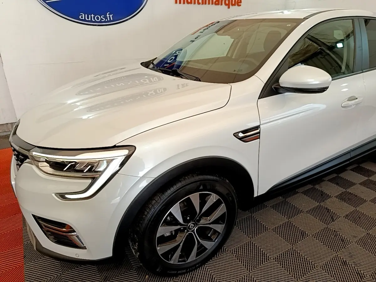 Renault Arkana blanc en vue 3/4 avant droit, avec phares LED et jantes alliage distinctives.