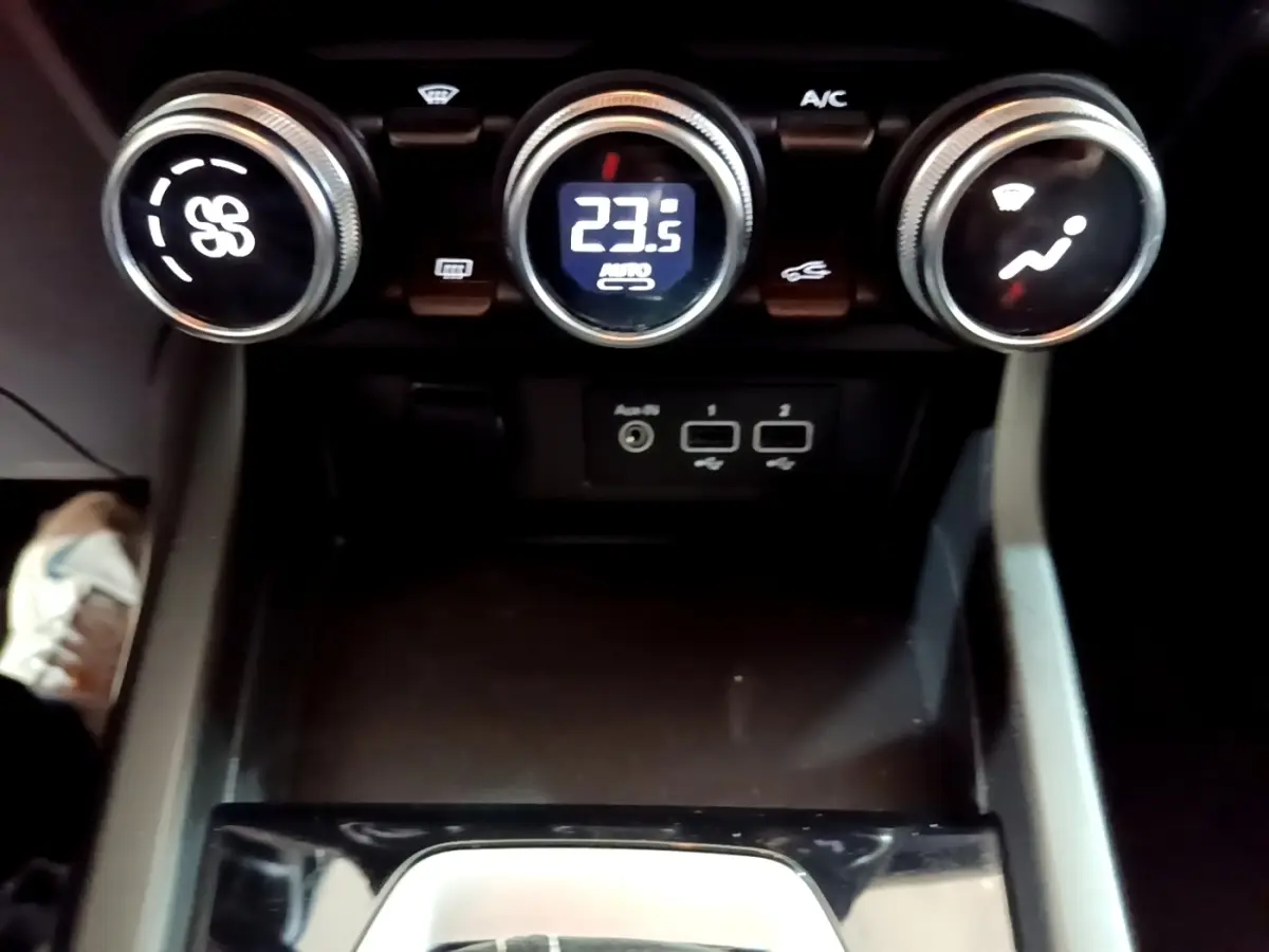 Gros plan sur la console centrale du Renault Arkana Evolution E-Tech 2023, montrant les commandes de climatisation et ports USB.