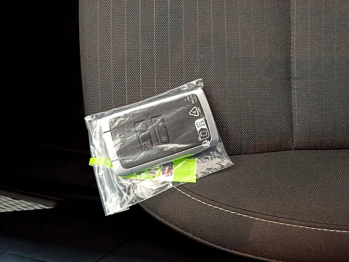 Gros plan sur la clé Renault Arkana Evolution E-Tech blanche posée sur un siège tissu gris foncé.