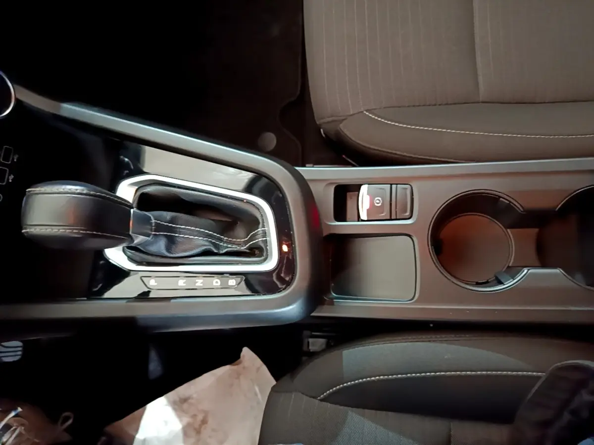 Vue plongeante sur la console centrale noire avec levier de vitesse automatique et frein à main électrique du Renault Arkana blanc.