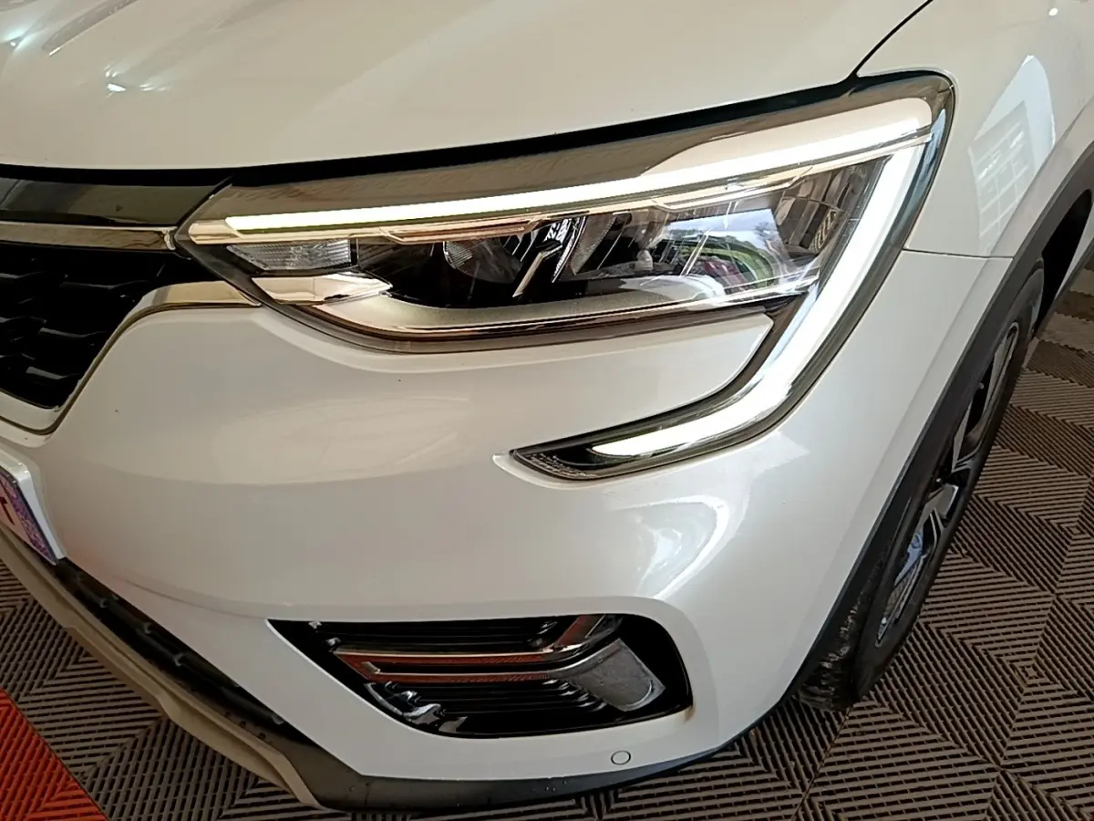 Gros plan sur l'avant droit blanc du Renault Arkana 2023, mettant en valeur le phare LED et la calandre noire.