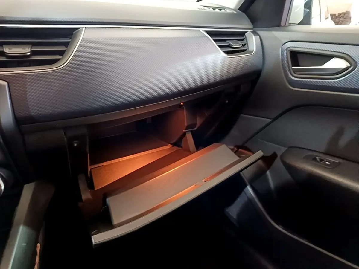 Vue intérieure côté passager du tableau de bord noir du Renault Arkana avec boîte à gants ouverte et éclairage intérieur.