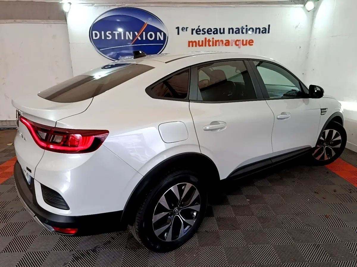 Renault Arkana blanc en 3/4 arrière droit, feux LED allumés et jantes alliage distinctives visibles.