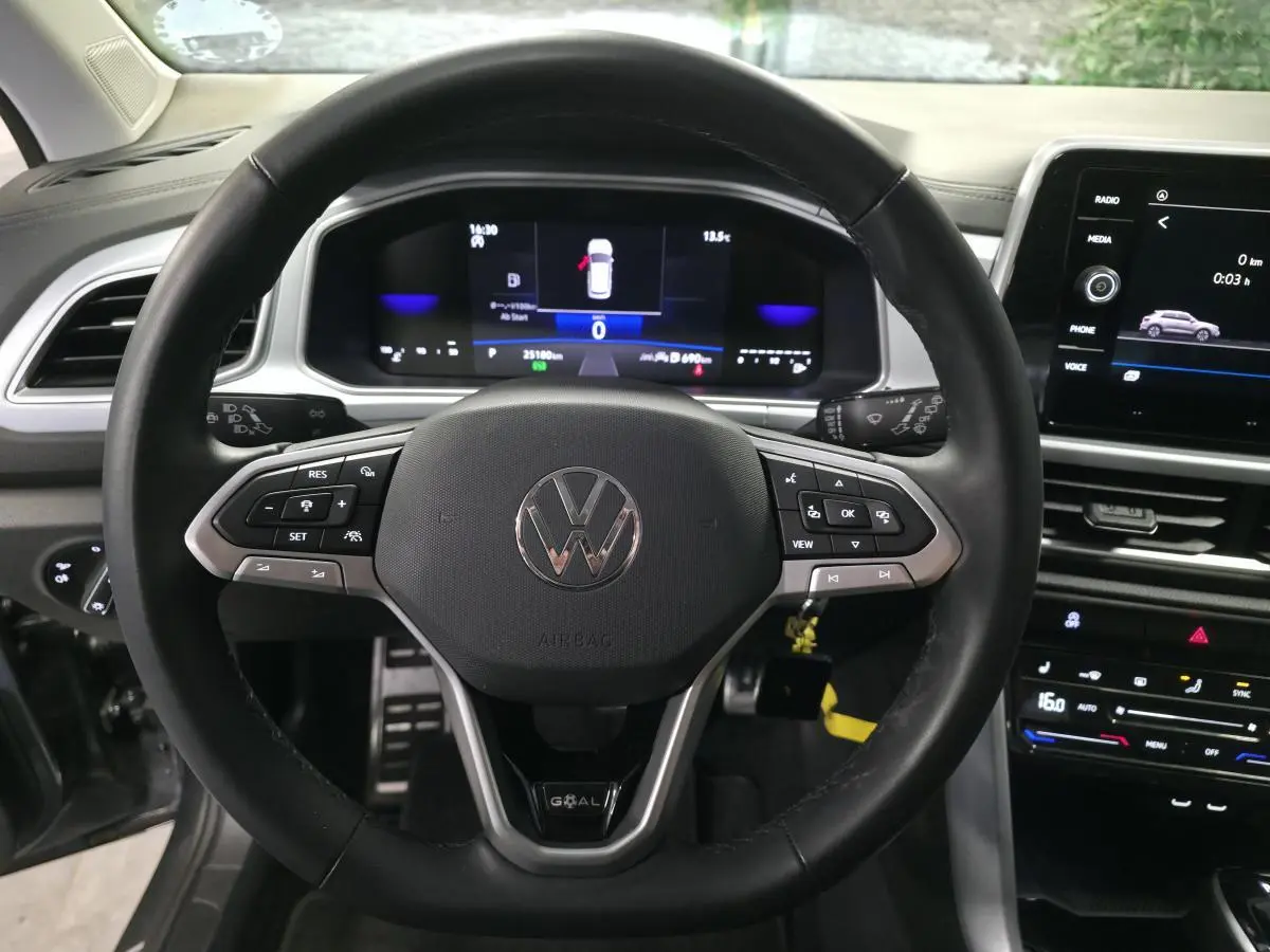 Vue intérieure centrée sur le volant noir du Volkswagen T-Roc gris avec tableau de bord digital et écran tactile.