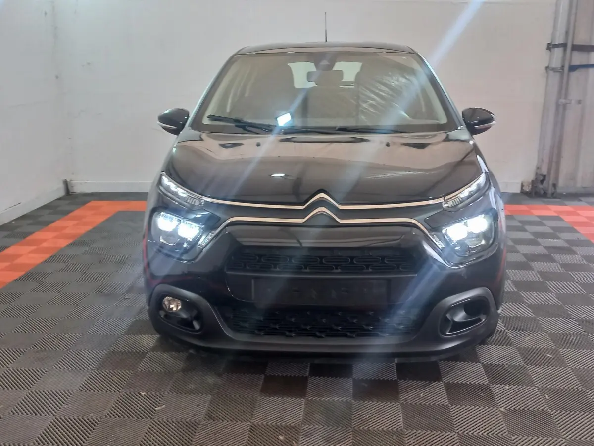 Vue frontale d'une Citroën C3 noire 2024 avec phares LED allumés dans un garage au sol damier.