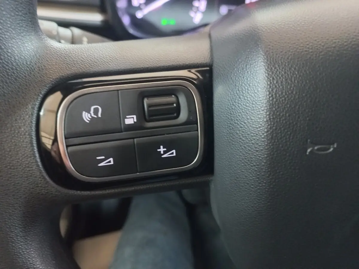 Gros plan sur les commandes multifonctions à gauche du volant noir de la Citroën C3 BlueHDi 2024.