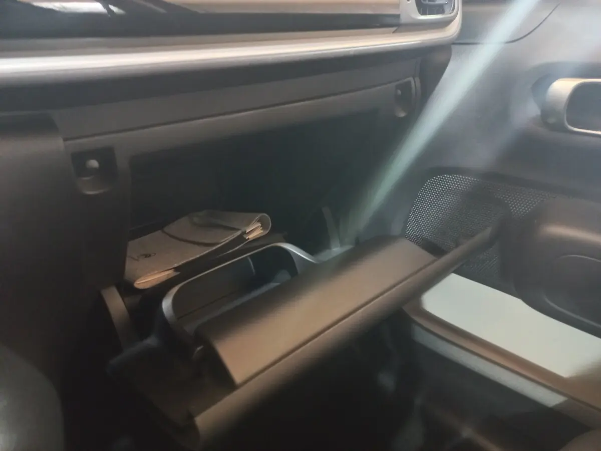Intérieur de la Citroën C3 2024 noir, vue sur la boîte à gants ouverte côté passager avec rangement et document visible.