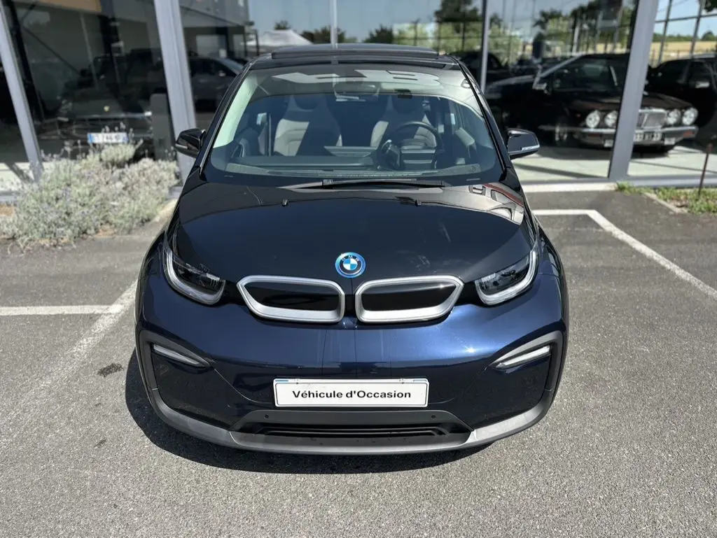Vue avant d'une BMW i3 électrique bleu foncé avec capot noir et plaque "Véhicule d'Occasion" visible.