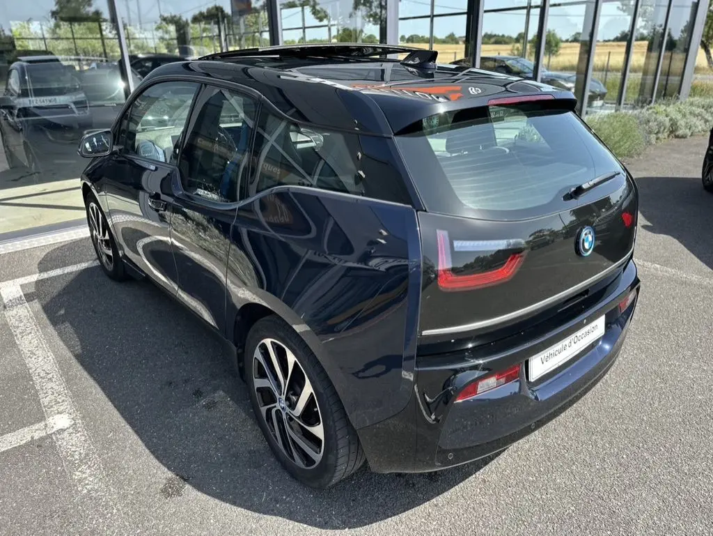 Vue 3/4 arrière droite d'une BMW i3 électrique bleue 2022 avec jantes stylisées et toit vitré en concession.