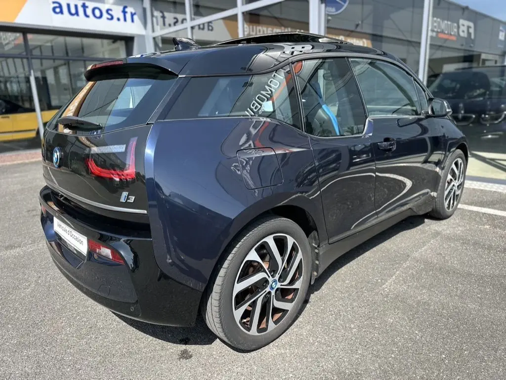 Vue 3/4 arrière droite d'une BMW i3 électrique bleue 2022 avec jantes distinctives et toit noir brillant.