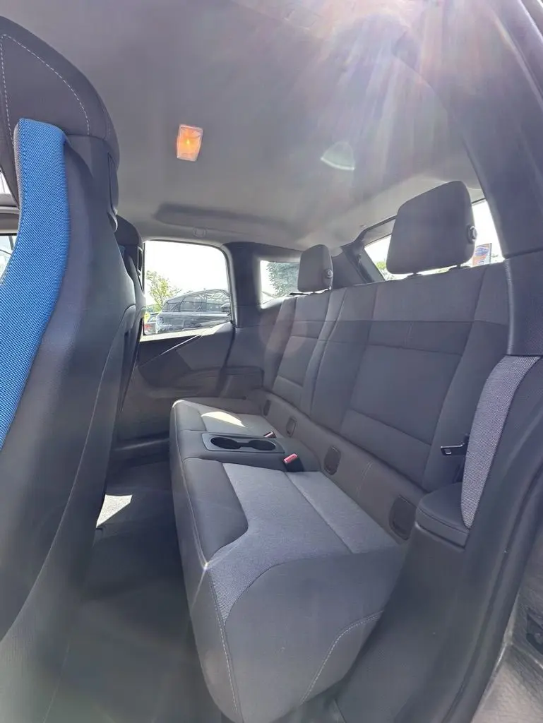 Vue intérieure arrière droite de la BMW i3 120 AH Edition Windmill avec sièges gris et bleu, lumière naturelle entrant par la fenêtre.