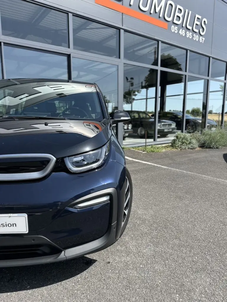 Vue 3/4 avant gauche d'une BMW i3 électrique bleue 2022 stationnée devant une vitrine de concession.