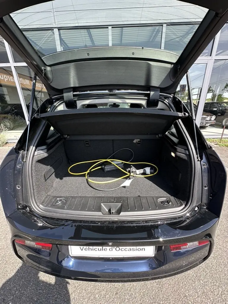 Vue arrière du coffre ouvert d'une BMW i3 bleue électrique 2022 avec câble de recharge visible à l'intérieur.