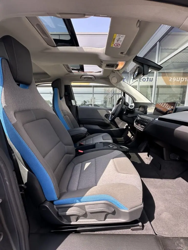 Intérieur de la BMW i3 2022 vue côté droit, sièges gris avec surpiqûres bleues et toit ouvrant panoramique.