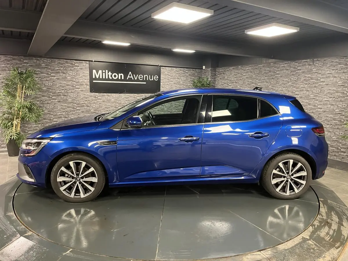 Profil côté gauche de la Renault Mégane hybride rechargeable bleu Iron avec jantes alliage 17 pouces en intérieur showroom.