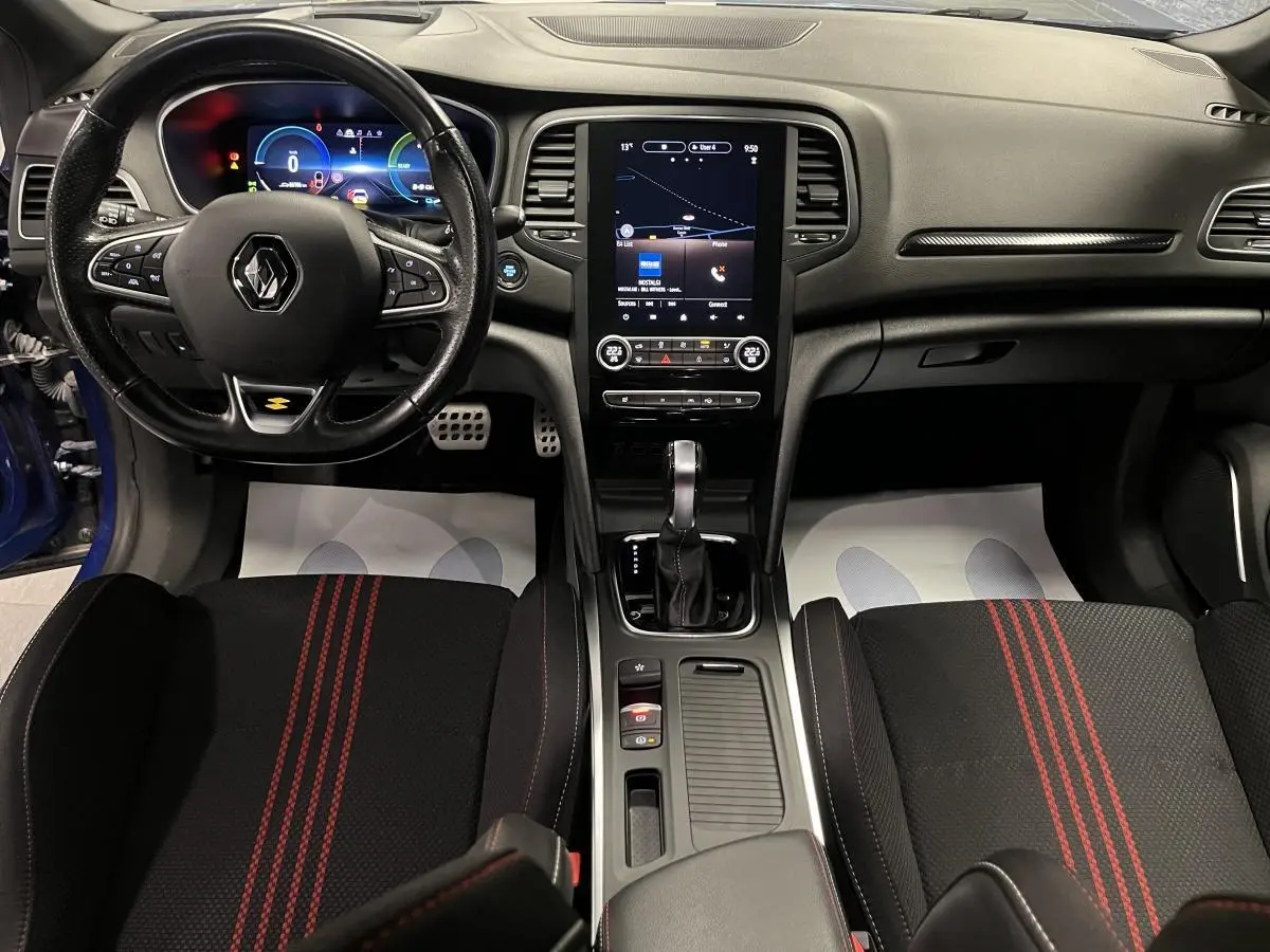 Intérieur Renault Mégane 1.6 E-Tech hybride, vue avant centrée sur tableau de bord, volant cuir R.S. Line et sièges noirs à surpiqûres rouges.