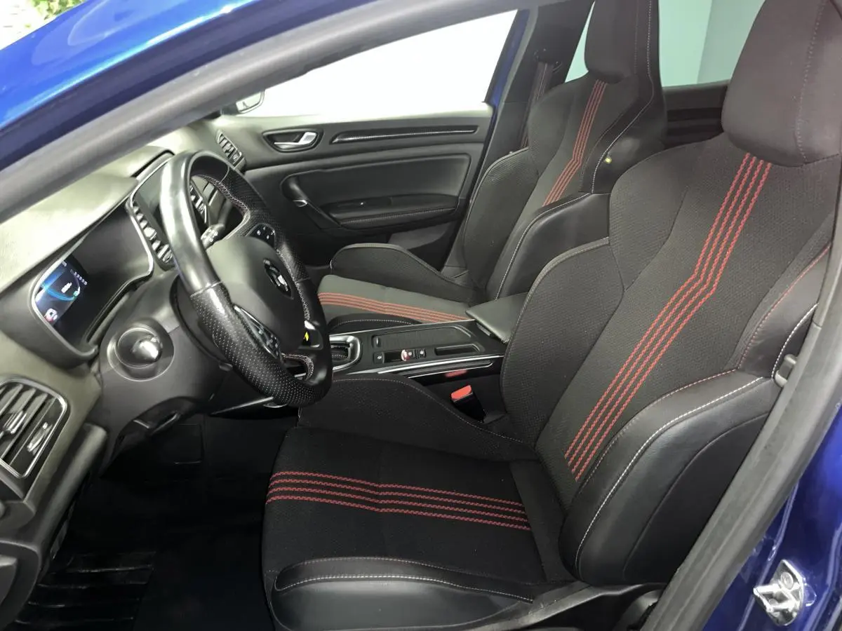 Vue intérieure côté conducteur de la Renault Mégane 1.6 E-Tech hybride bleue avec sièges sport noirs à surpiqûres rouges.