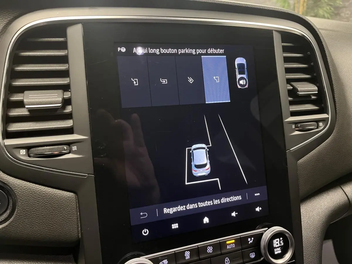 Écran tactile central de la Renault Mégane hybride bleue affichant l'assistance au stationnement en vue intérieure.