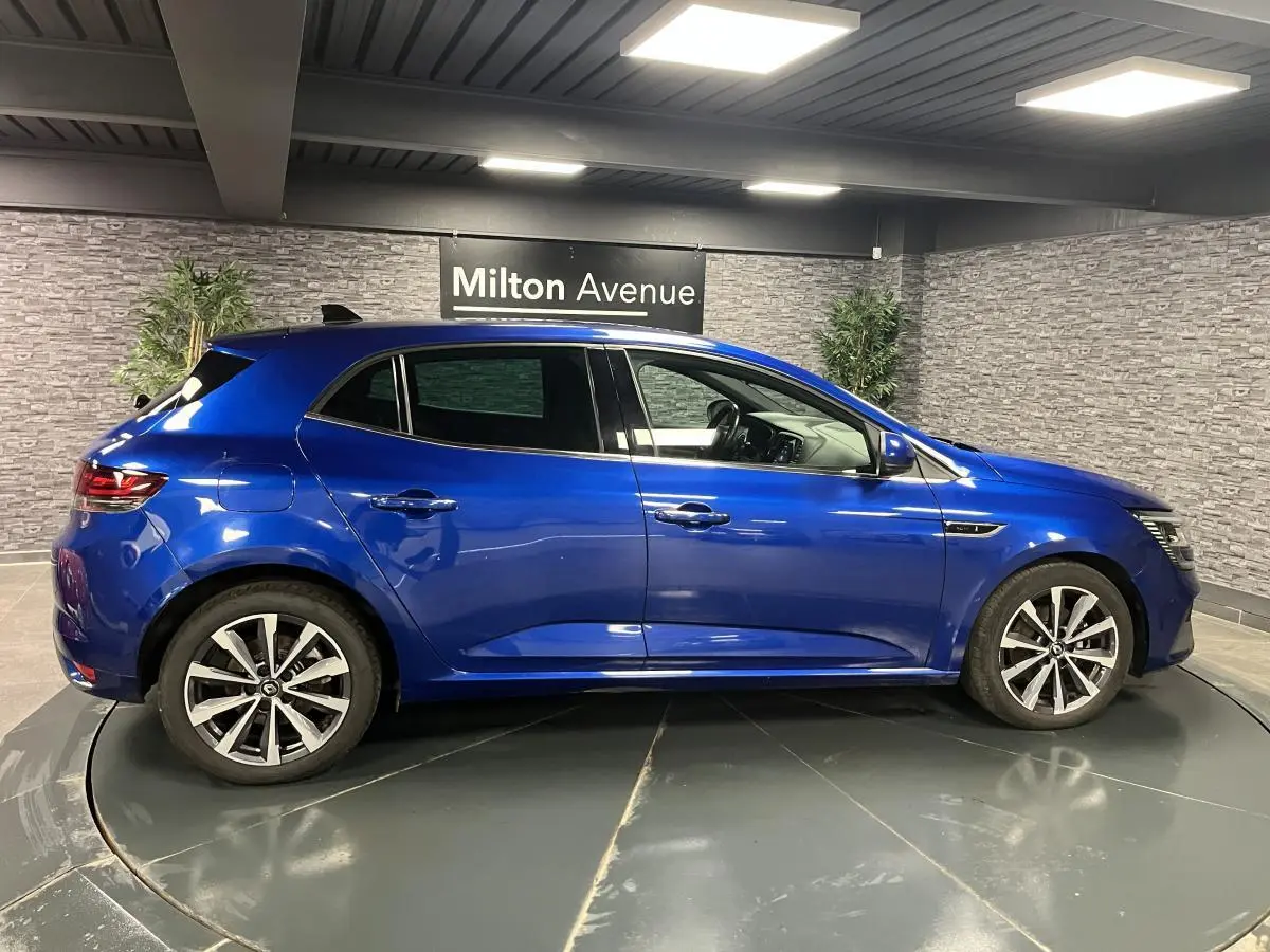 Profil côté gauche de la Renault Mégane hybride rechargeable bleu Iron avec jantes alliage 17 pouces en intérieur showroom.