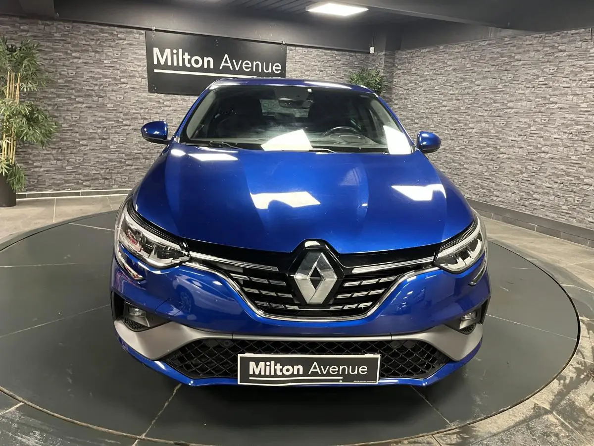 Vue frontale d'une Renault Mégane bleu Iron avec calandre chromée et phares LED en intérieur showroom.