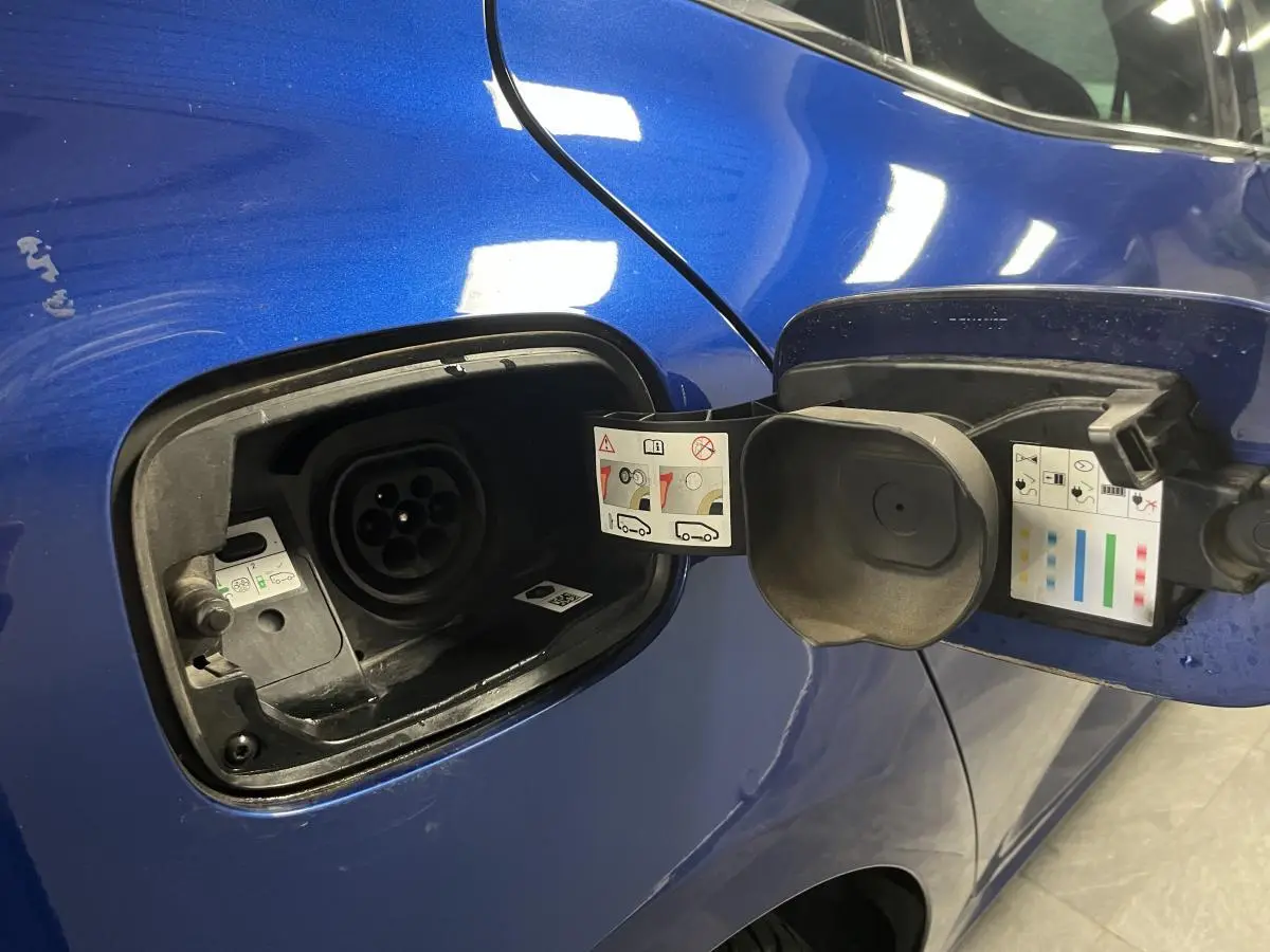 Prise de recharge ouverte côté gauche sur Renault Mégane hybride rechargeable bleu Iron, détails des consignes visibles.