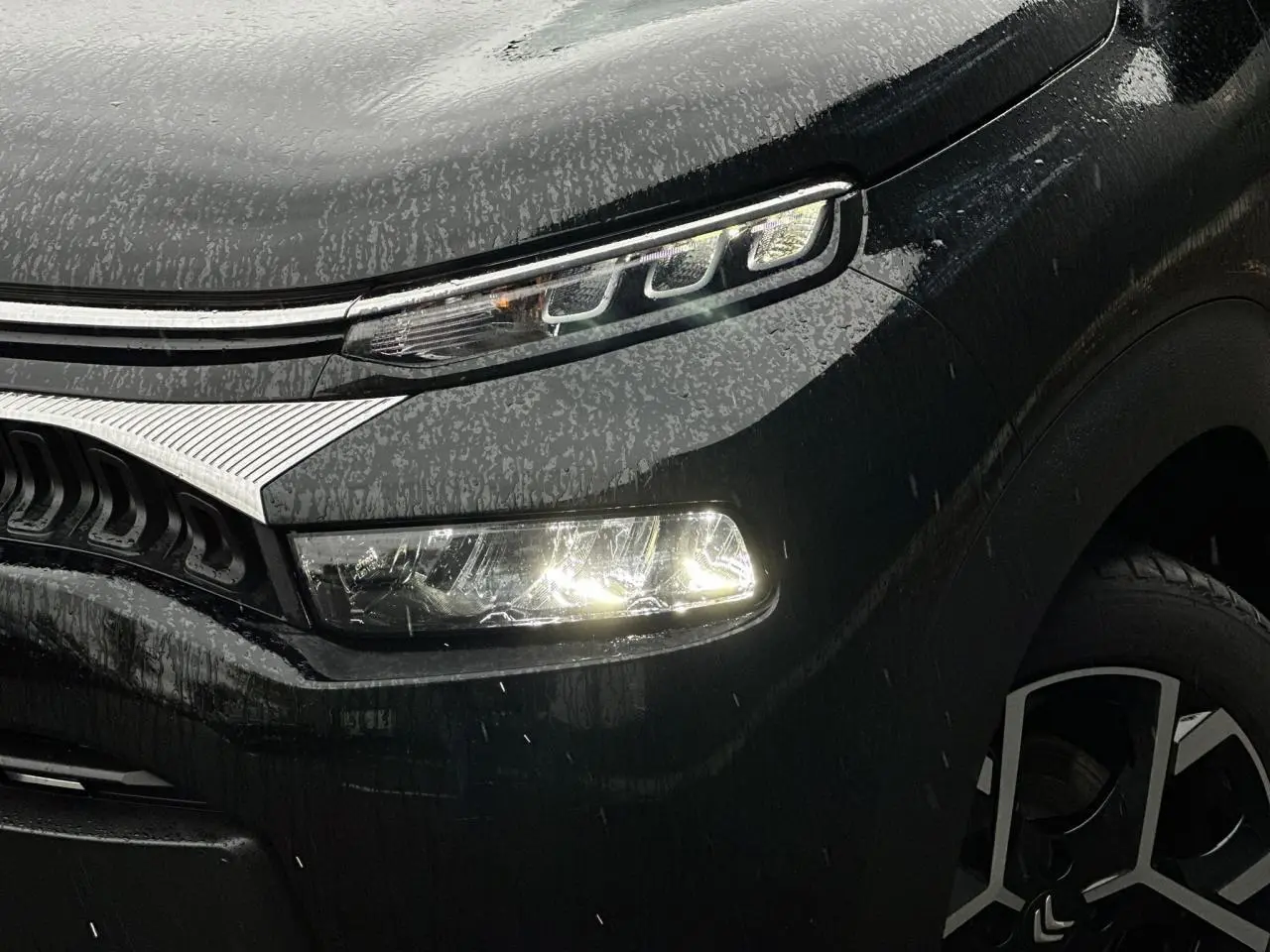 Gros plan sur l'avant droit noir Perla du Citroën C3 Aircross 2024 avec phares LED allumés et jante alliage 17'' distinctive.