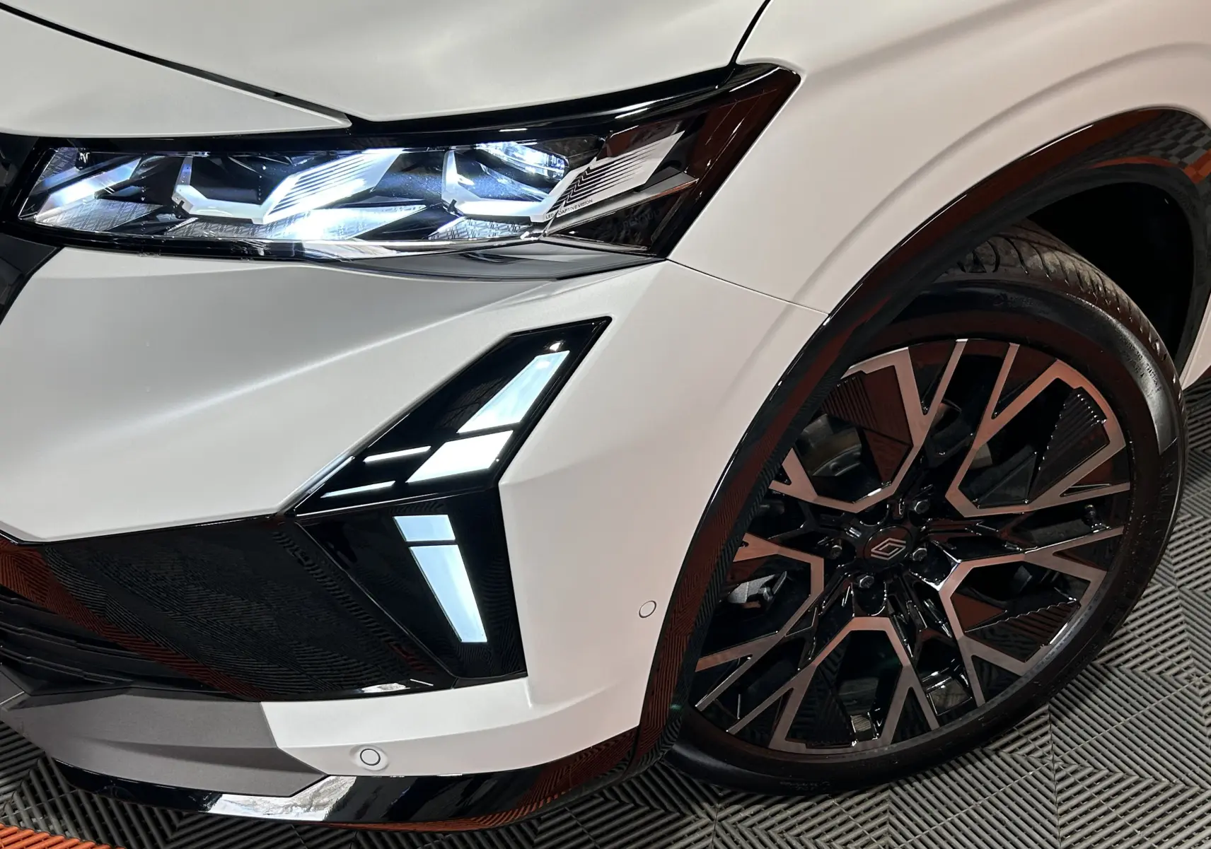 Gros plan sur l'avant droit du Renault Austral blanc nacré satin, mettant en valeur le phare LED et la jante alliage bicolore.