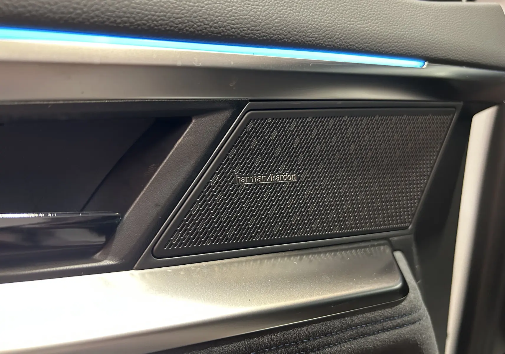 Gros plan sur la porte côté gauche du Renault Austral blanc nacré, mettant en valeur l'enceinte Harman Kardon et l'éclairage d'ambiance bleu.