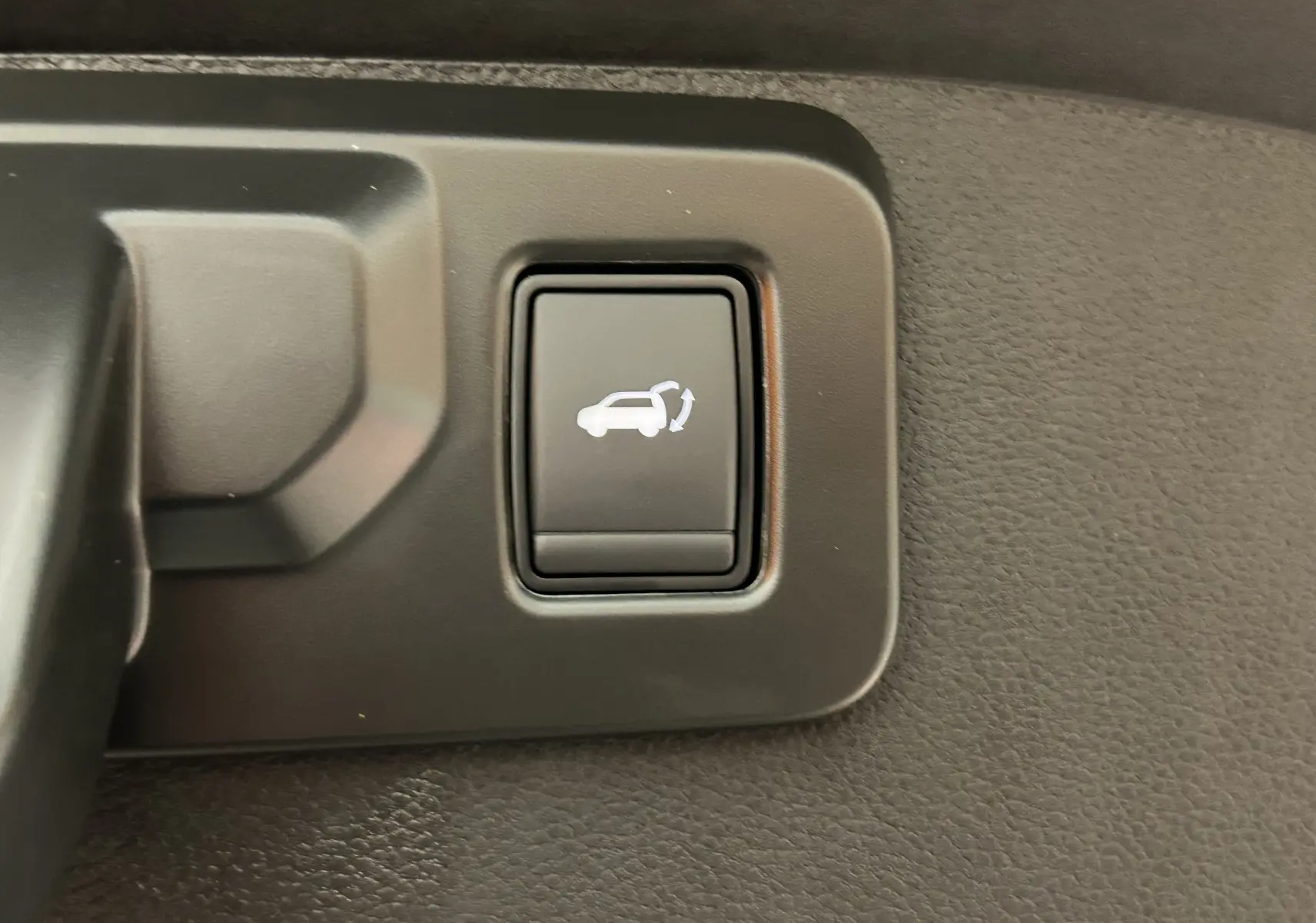 Bouton intérieur noir avec symbole blanc d'ouverture du hayon sur Renault Austral blanc nacré, vue rapprochée.