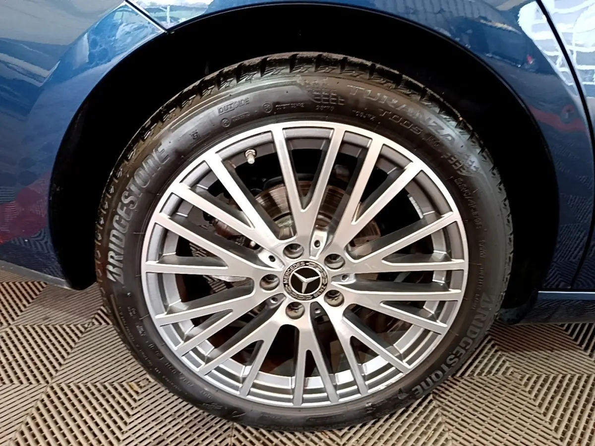 Gros plan sur la jante alu multi-branches argentée d’une Mercedes CLA 180 d Business Line, carrosserie bleu foncé visible.