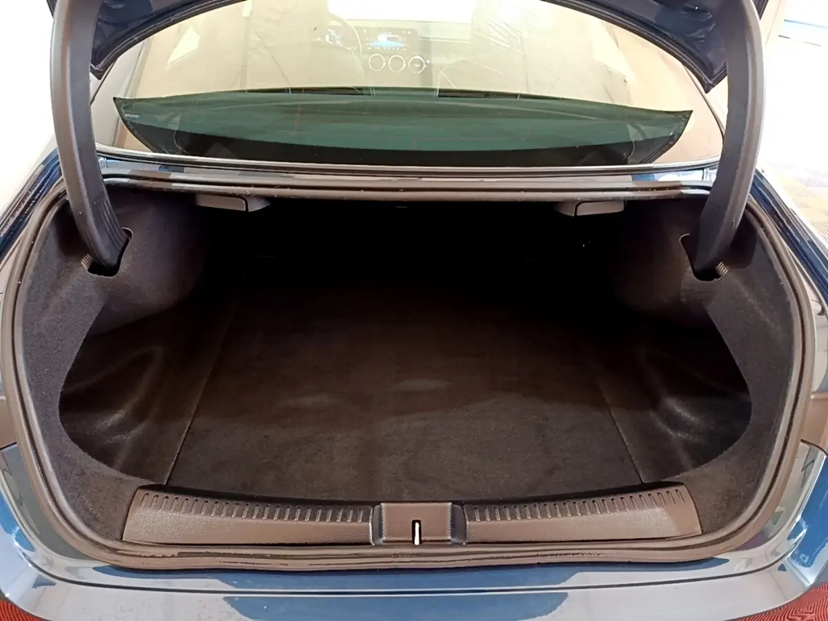 Coffre ouvert vu de l'arrière d'une Mercedes CLA 180 d Business Line blanche, intérieur noir et moquette propre.