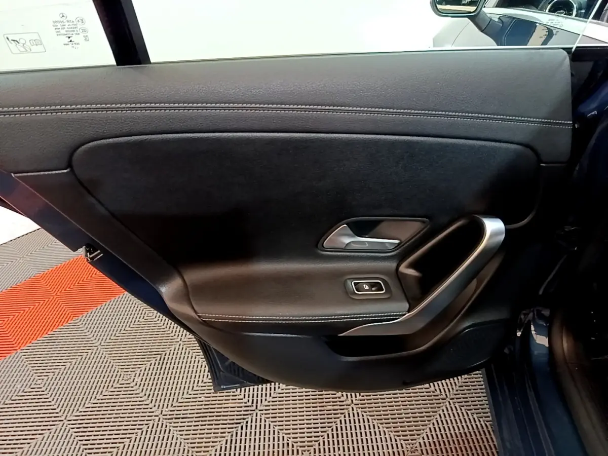 Vue intérieure de la porte arrière gauche noire de la Mercedes CLA 180 d Business Line 2021 avec poignée alu et commande de fenêtre.
