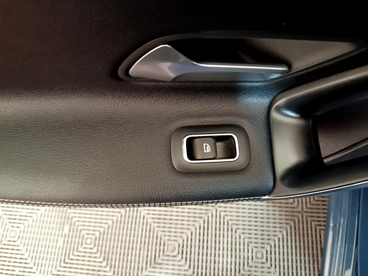 Gros plan sur la commande de lève-vitre côté conducteur en cuir noir avec surpiqûres blanches dans une Mercedes CLA 180 d blanche.