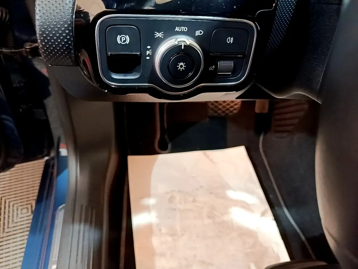 Gros plan sur le panneau de commande des phares et frein à main électrique dans l'habitacle d'une Mercedes CLA 180 d blanche.