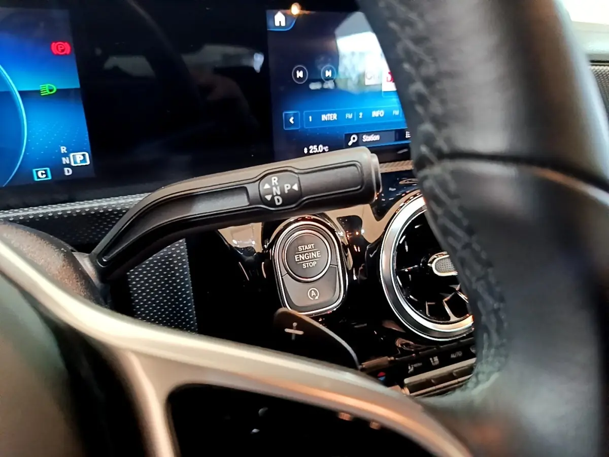 Gros plan intérieur sur le volant cuir et alu d’une Mercedes CLA 180 d blanche, avec bouton démarrage et écran digital.