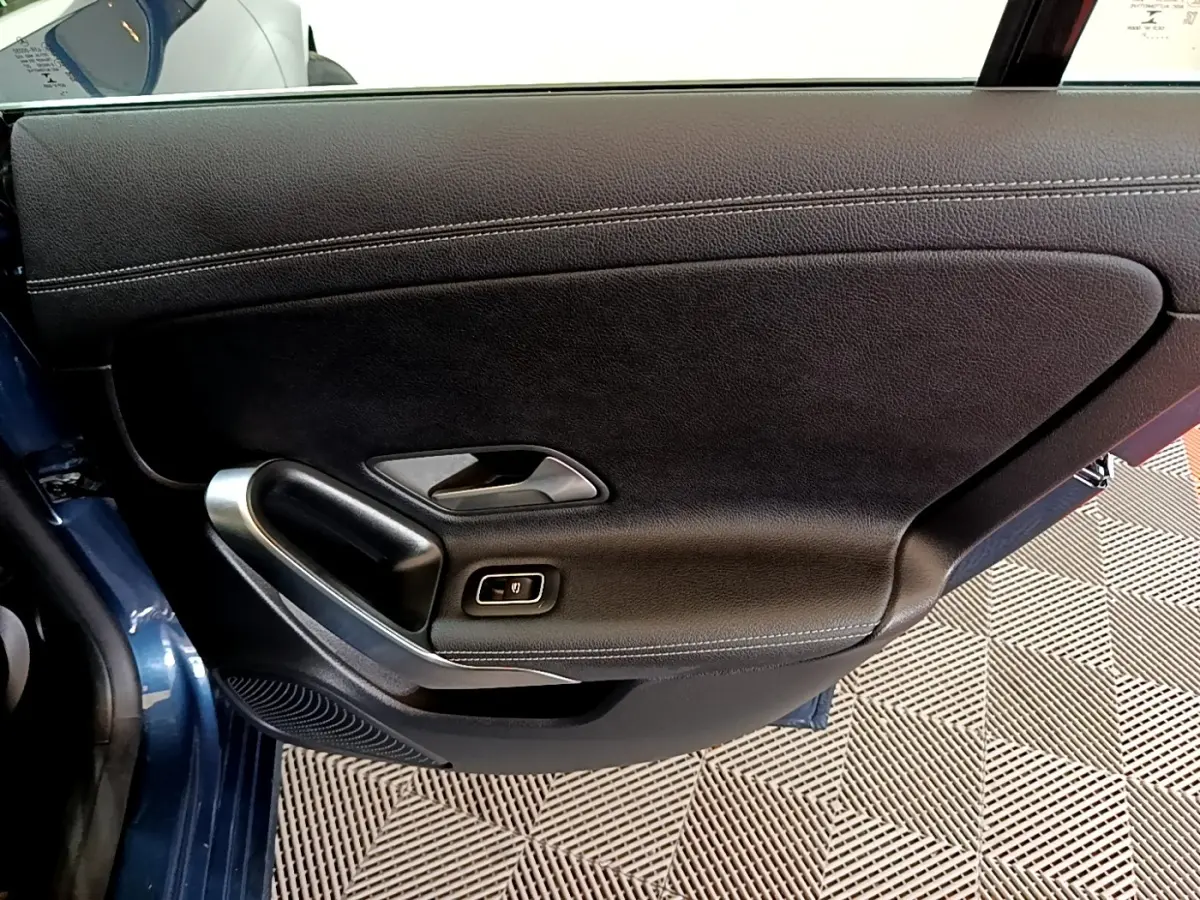 Gros plan sur la porte intérieure côté gauche d'une Mercedes CLA 180 d Business Line blanche, avec poignée alu et cuir noir.