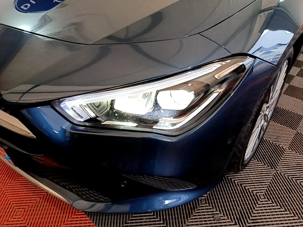 Gros plan sur le phare avant droit allumé d'une Mercedes CLA 180 d Business Line bleu foncé, avec jante visible.