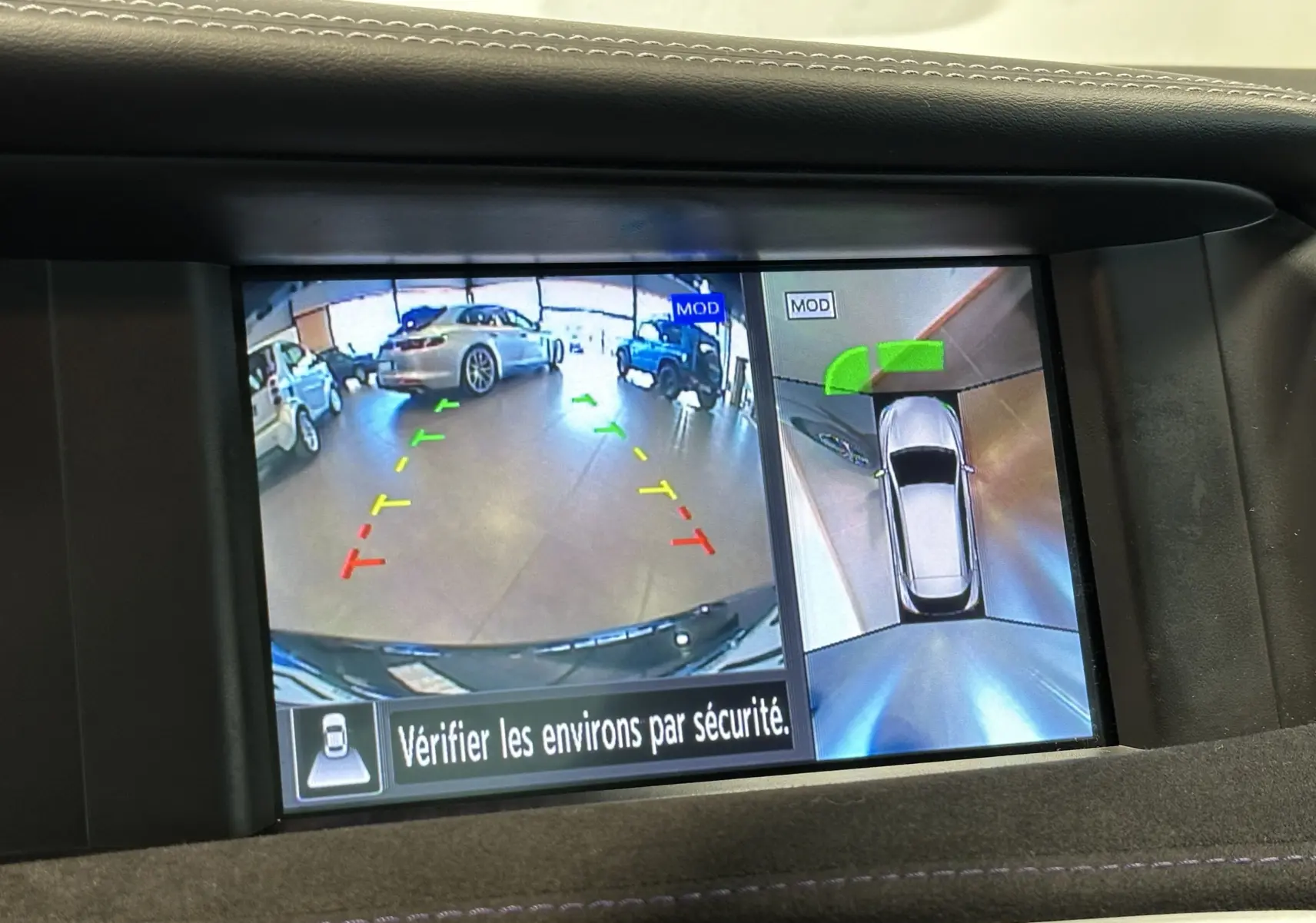Vue écran caméra de recul et vue aérienne d'une Infiniti Q30 noire en stationnement intérieur avec repères colorés.