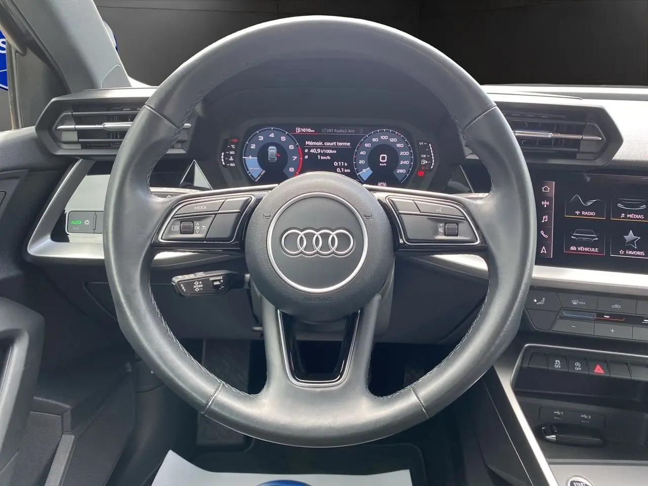 Vue centrée sur le volant noir de l'Audi A3 Sportback 30 TFSI 110 S-Line avec tableau de bord numérique et écran tactile.