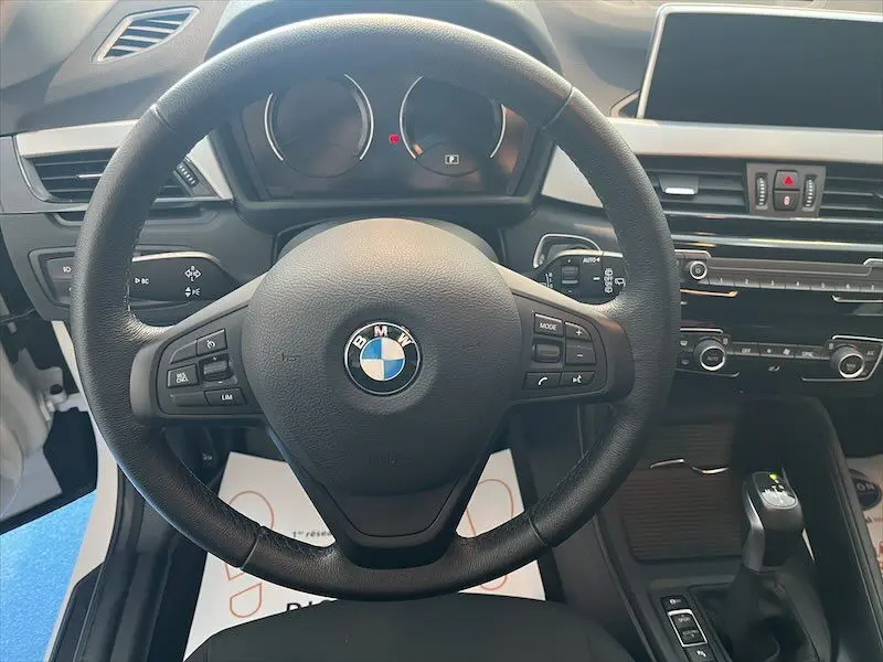 Vue centrée sur le volant BMW noir et le tableau de bord du BMW X1 blanc alpin, avec console centrale moderne.