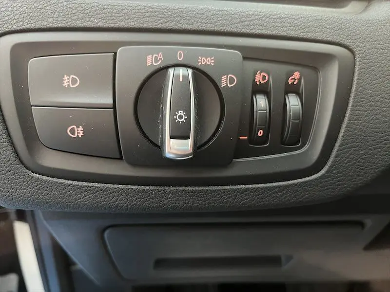 Gros plan sur le panneau de commande des phares et réglages lumineux du BMW X1 XDRIVE 25E blanc alpin, intérieur noir.