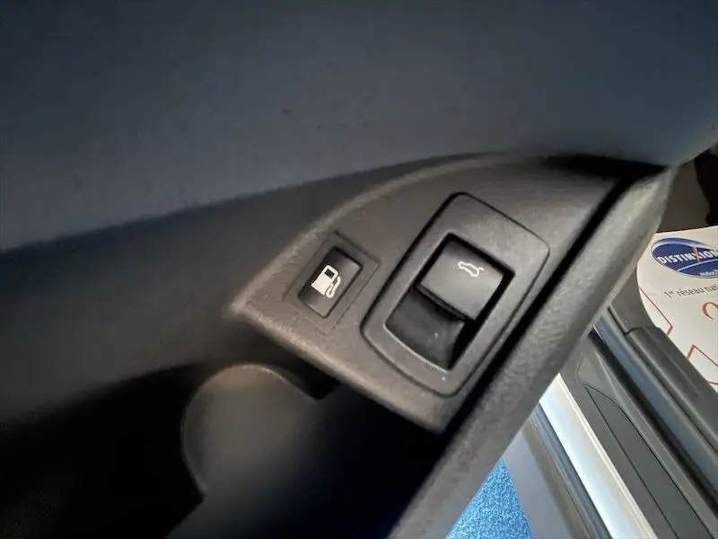 Détail intérieur montrant les commandes d'ouverture du réservoir et du coffre sur un BMW X1 blanc alpin 2021.