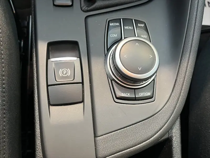 Gros plan sur la molette de commande multimédia et frein à main électronique du BMW X1 XDRIVE blanc Alpine, intérieur moderne.