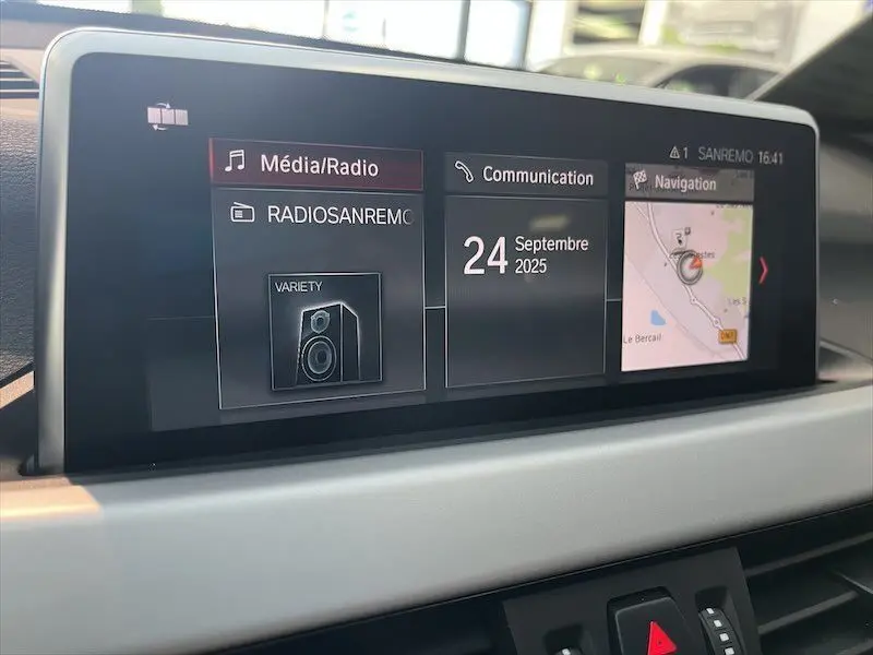 Écran central du tableau de bord du BMW X1 XDRIVE 25E blanc, affichant radio, communication et navigation.