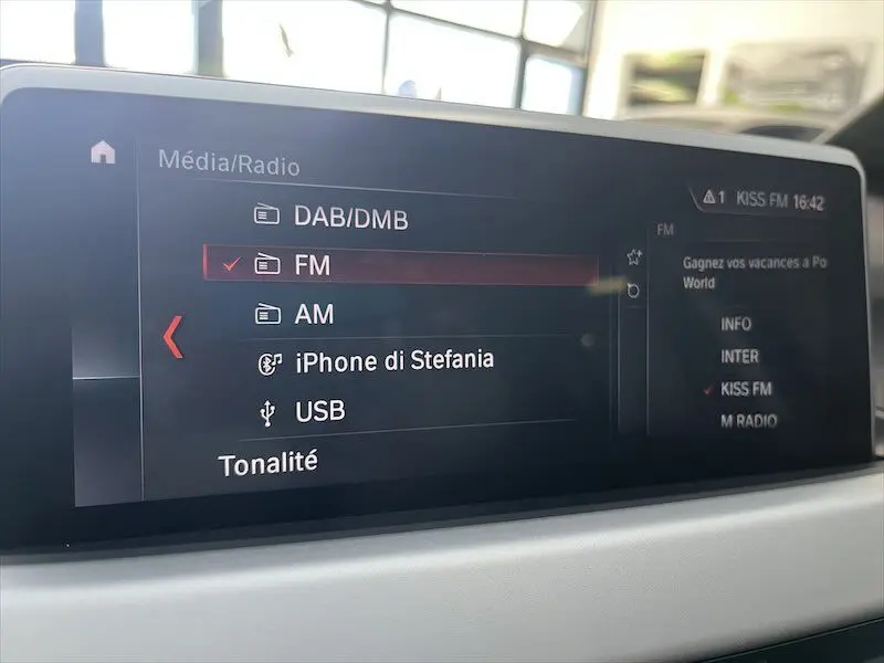 Écran multimédia du BMW X1 25E blanc, affichant les options radio FM, AM, DAB/DMB et connexion iPhone.