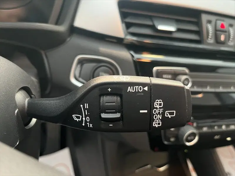 Gros plan sur la commande des essuie-glaces noire à gauche du volant dans l'habitacle d'un BMW X1 blanc.