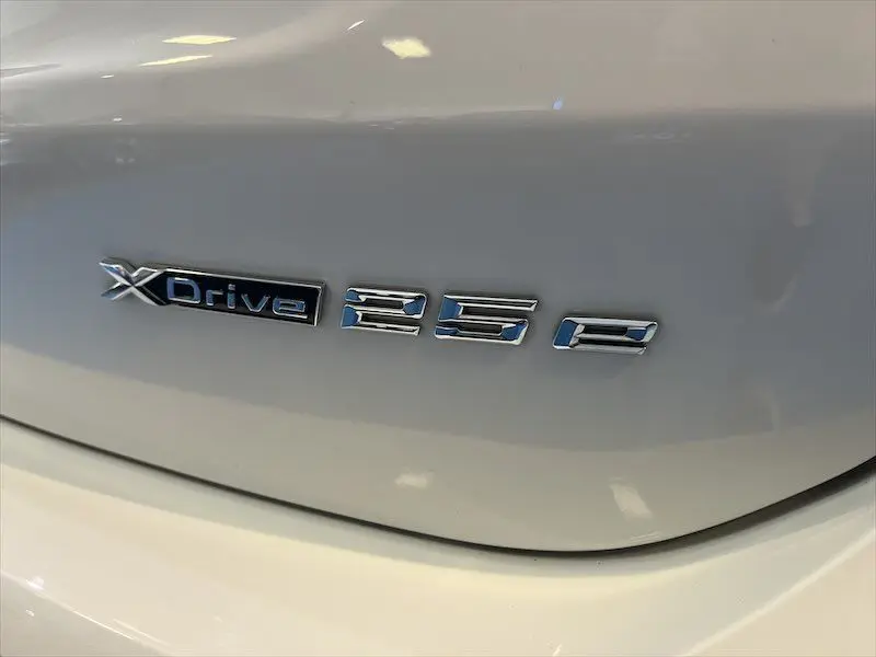 Gros plan sur l'emblème XDrive 25e argenté sur la carrosserie blanche alpin d'un BMW X1 hybride rechargeable.