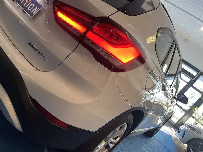 Vue 3/4 arrière droite d'un BMW X1 XDRIVE blanc alpin avec feu arrière allumé en intérieur showroom.